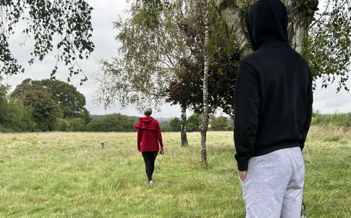 Man in hoodie watching lady walking her dog