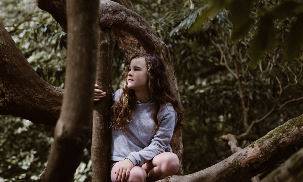 Young girl crouched among trees